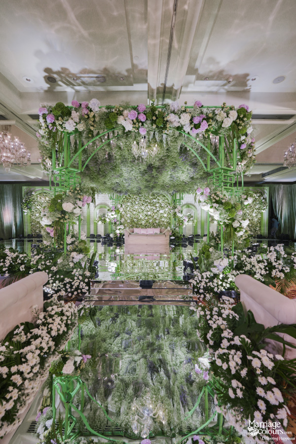 Vertical view of a luxurious wedding stage featuring a reflective mirrored aisle and extensive white flowers.