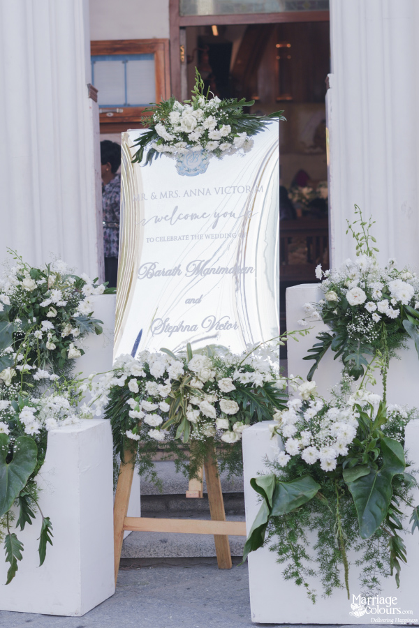 Elegant wedding welcome sign displayed on a wooden easel and decorated with white floral arrangements.