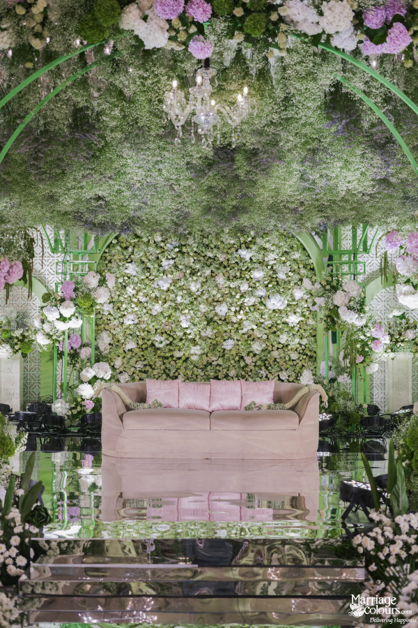 Close-up of a luxurious wedding stage featuring a blush sofa, floral wall, and mirrored floor.