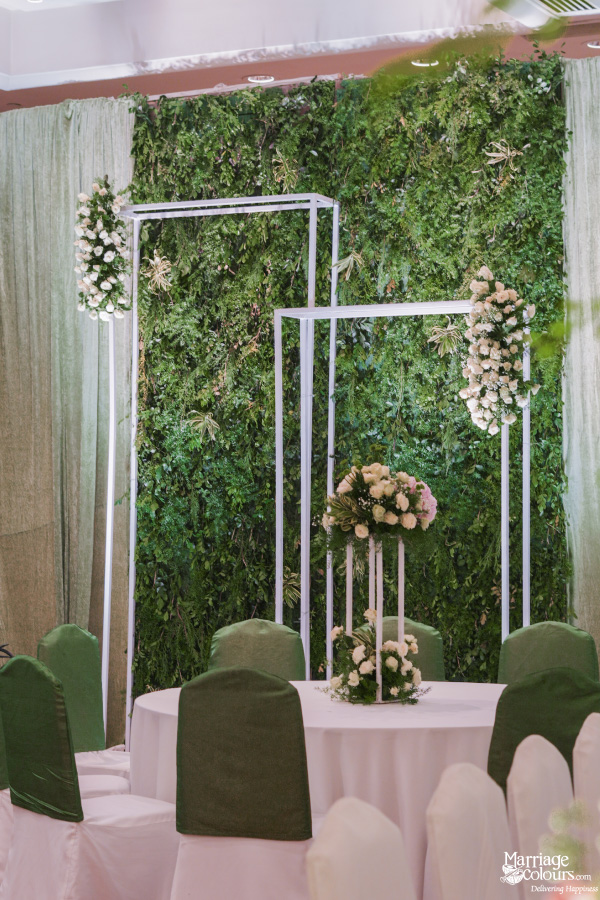 Wedding reception dining table setting against a lush, vertical greenery wall backdrop with white frames.