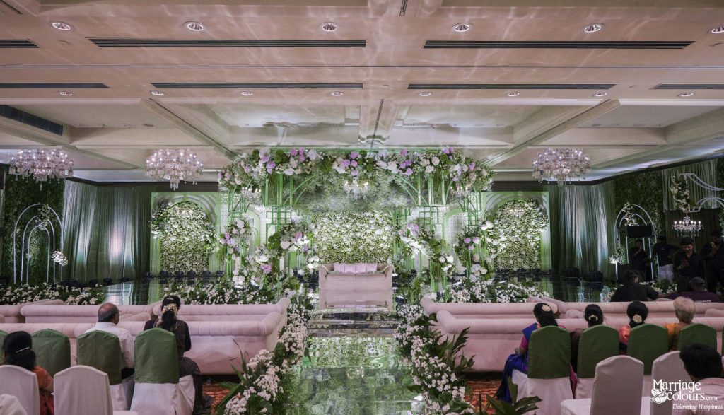 A lavish wedding reception stage decorated with extensive green foliage and white floral arrangements.
