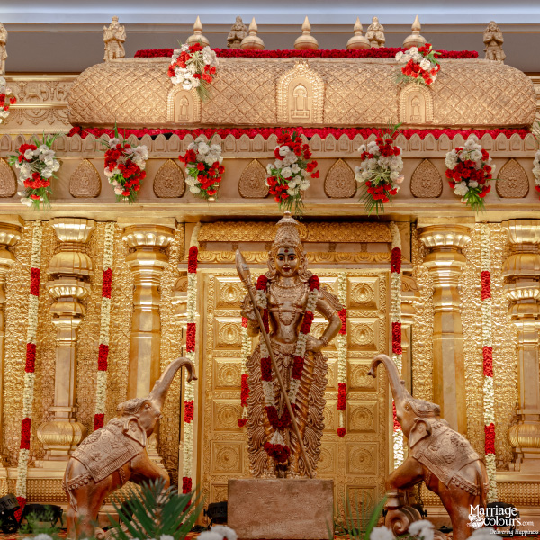 Close-up of a traditional South Indian wedding stage with gold decor and a deity statue.