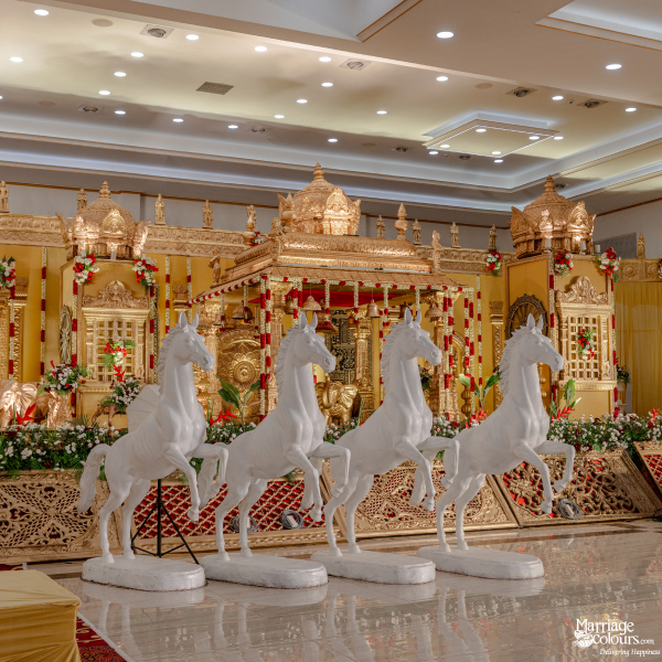 Four rearing white horse statues standing in front of an elaborate traditional gold wedding stage.