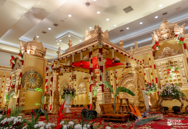 Wide view of a grand, elaborate South Indian wedding mandap featuring a central canopy and gold carvings.