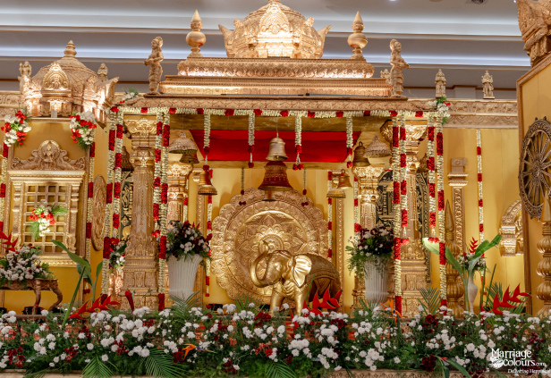 Magnificent, ornate South Indian wedding stage decorated primarily in gold, red, and white florals.