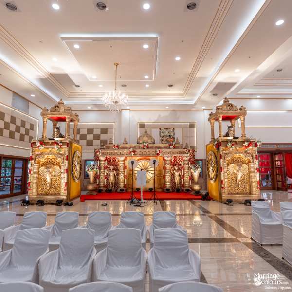 Wide view of a grand ballroom set up with white chairs facing an elaborate traditional Hindu wedding stage.
