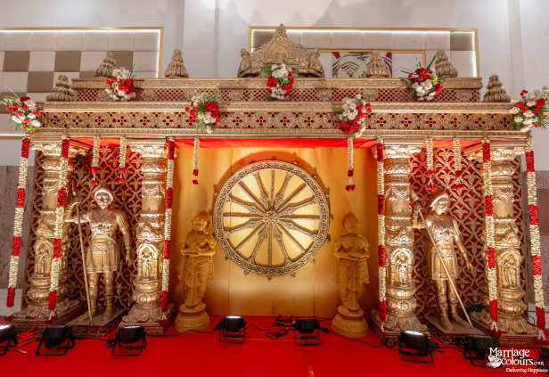 Traditional Hindu wedding stage decorated with gold carvings, floral garlands, and religious figures.