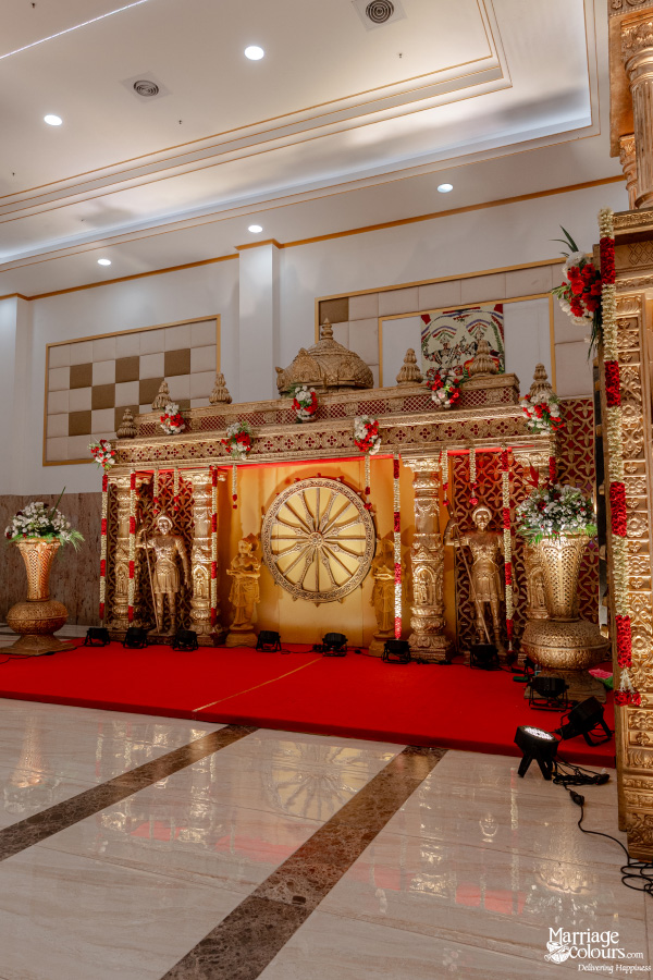 Vertical view of a traditional gold and red wedding stage with a majestic arch and golden figures.
