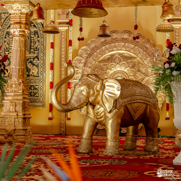 Close-up of a stunning golden elephant statue in front of an ornate wedding stage backdrop.