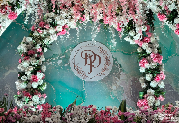 Close-up of pink and white floral archway with monogram against a teal marble backdrop.