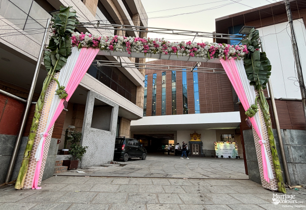 Event entrance gate decorated with pink and white fabric, banana leaves, and flowers.