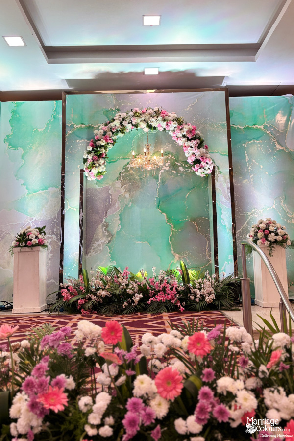 Stage foreground with pink and white flowers and teal marble-patterned backdrop archway.