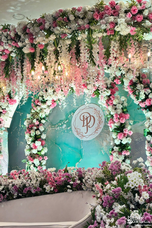 Close-up of pink and white floral archway with monogram against a teal marble backdrop.