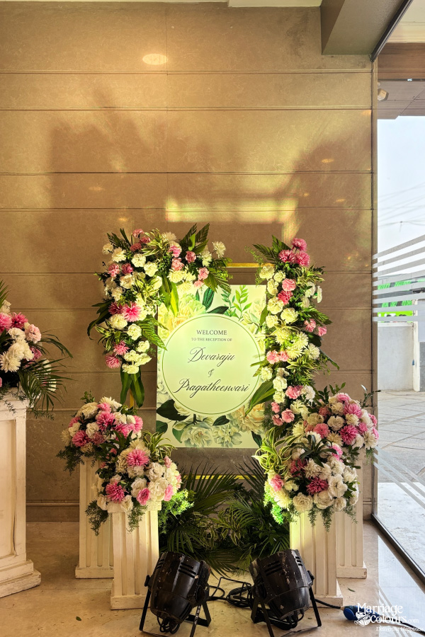 Reception welcome sign with floral columns for "Devaraja & Pragatheeswari" indoors.