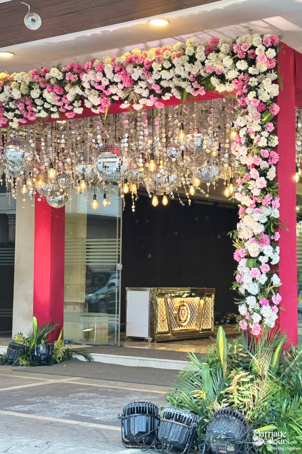 Event entrance decorated with disco balls, yellow lights, and pink and white flowers.
