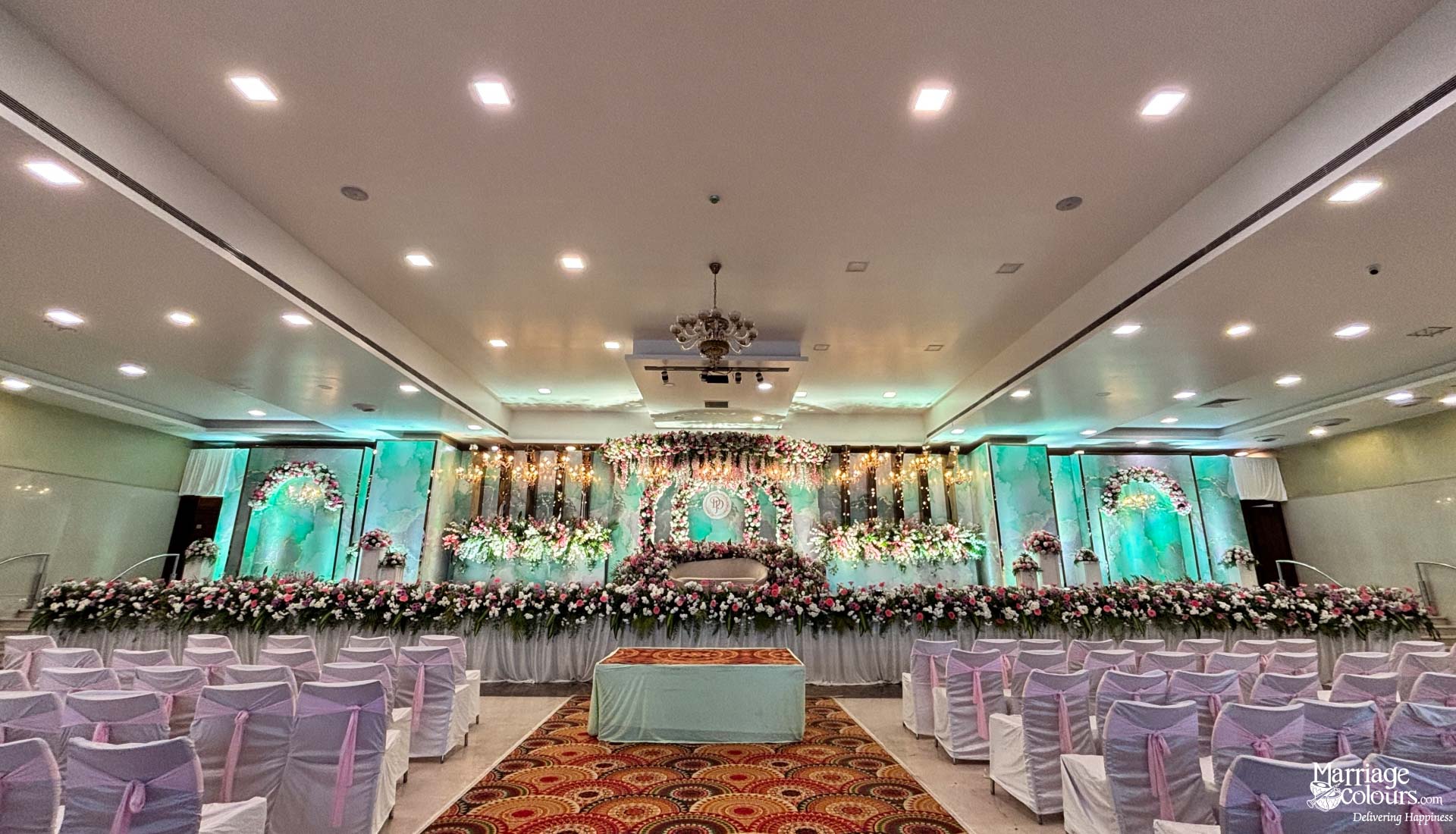 Wide view of grand hall with white and pink chairs facing a modern floral stage.