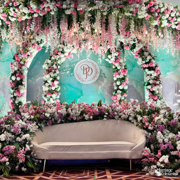 Modern stage couch and archway surrounded by pink and white flowers against a teal backdrop.