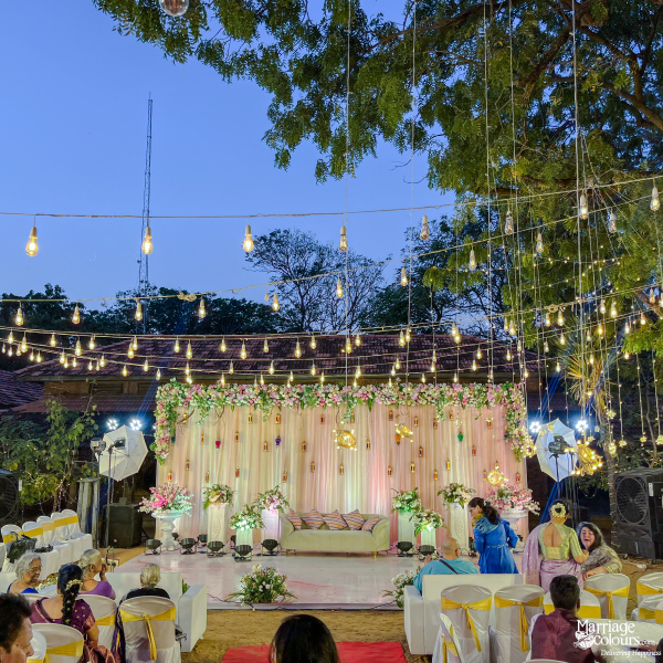 Wide shot of an elegant outdoor wedding reception with a floral stage and string light canopy.