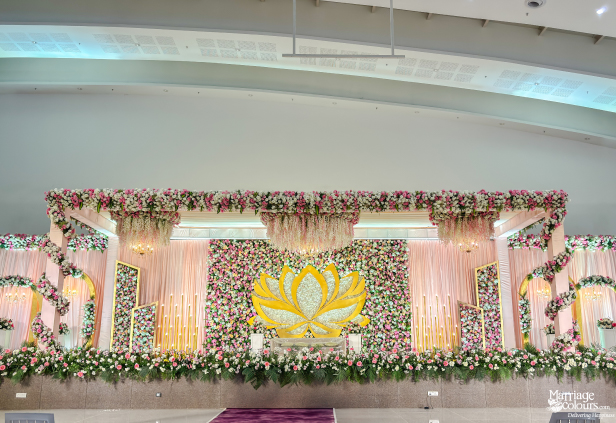 Elaborate indoor wedding stage with a massive pink and white floral wall and central golden lotus.