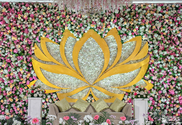 Wedding stage featuring a dense floral wall backdrop, large golden lotus cutout, and seating sofa.