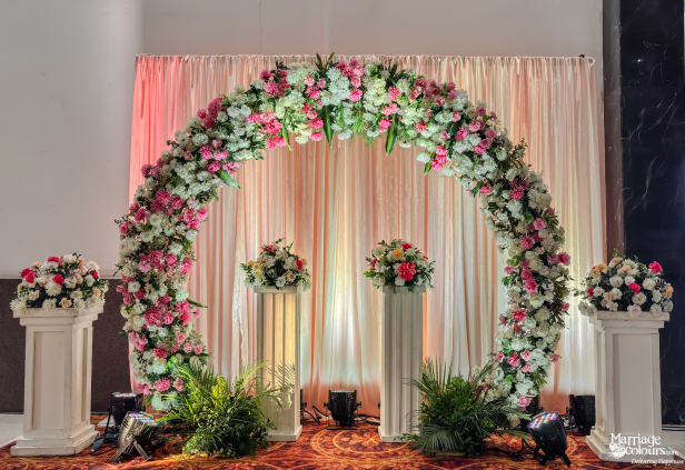 Wedding reception photo booth featuring a dense pink and white floral arch against pink draped curtains.