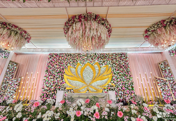 Grand wedding stage featuring a pink flower wall, golden lotus, and cascading pink and white floral chandeliers.