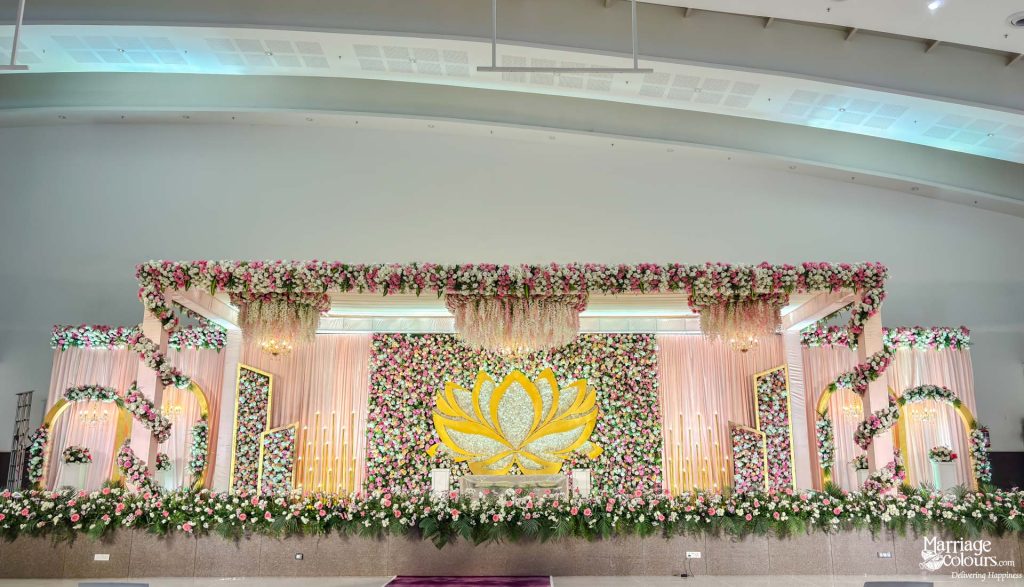 Elaborate indoor wedding stage decoration with a yellow lotus centerpiece and abundant pink flowers