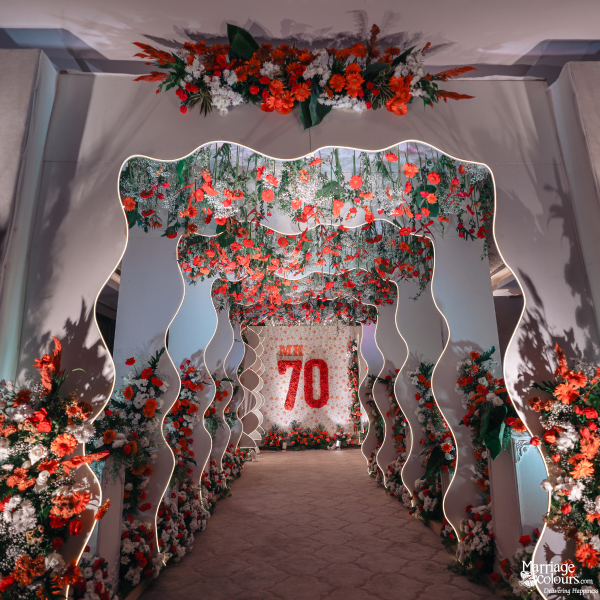 Illuminated entrance tunnel with overhead red flowers leading to an 'MK 70' backdrop.