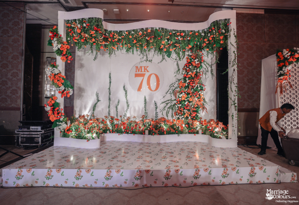 Empty white stage floor with floral pattern, 'MK 70' sign, and orange flower decor.