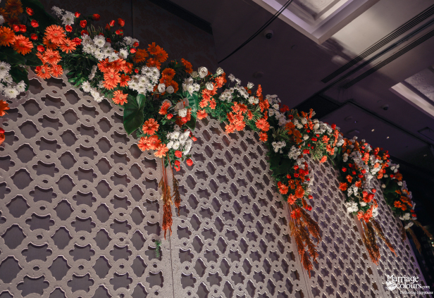 Close-up of a white patterned wall adorned with vibrant orange and white floral garlands.