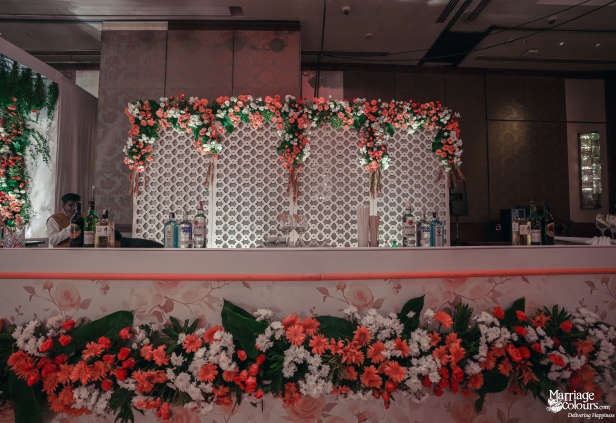 Event bar counter with white patterned backdrop and orange and white floral decoration.
