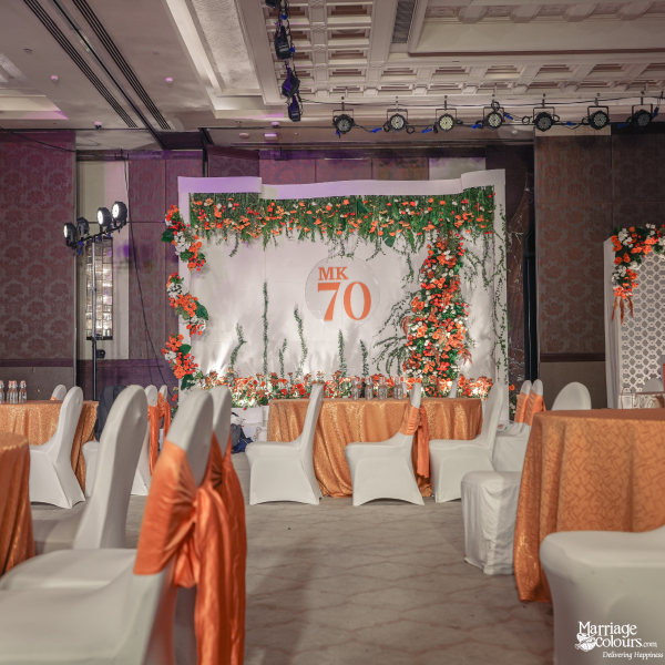 Event tables with orange and white decor leading to the floral-covered 'MK 70' stage.