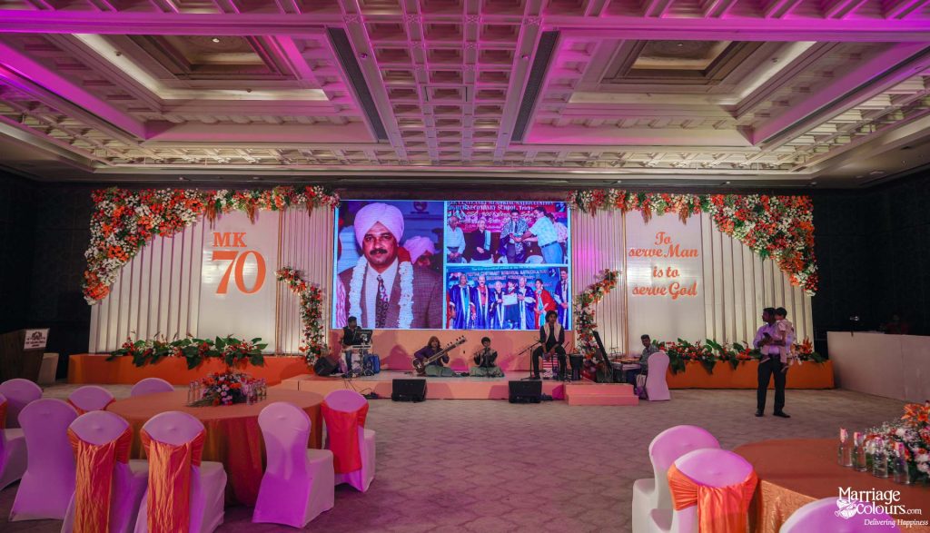 Celebration stage with live band, large screen, and orange floral decor.