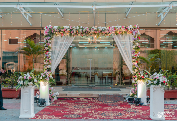 Elegant wedding entrance arch with white sheer drapes, pink and white flowers, and red carpet.