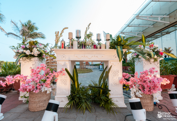 Detailed white stone altar decorated with candles, pink and white flowers, and lush green foliage.