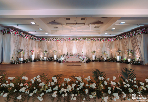 Wide-shot of a lavish wedding reception stage with a central sofa and pink and white floral border.