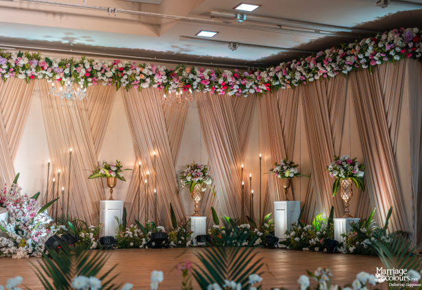 Elegant wedding reception backdrop with draped peach fabric, rich flowers, and warm candle lighting.