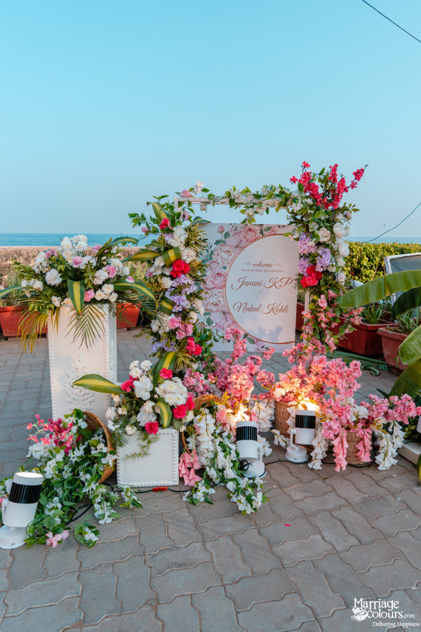 Seaside wedding welcome sign beautifully framed by dense pink, red, and white floral arrangements.