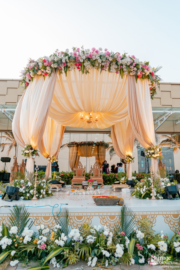 Elegant outdoor wedding mandap with a peach draped canopy, beautiful flowers, and traditional seating.