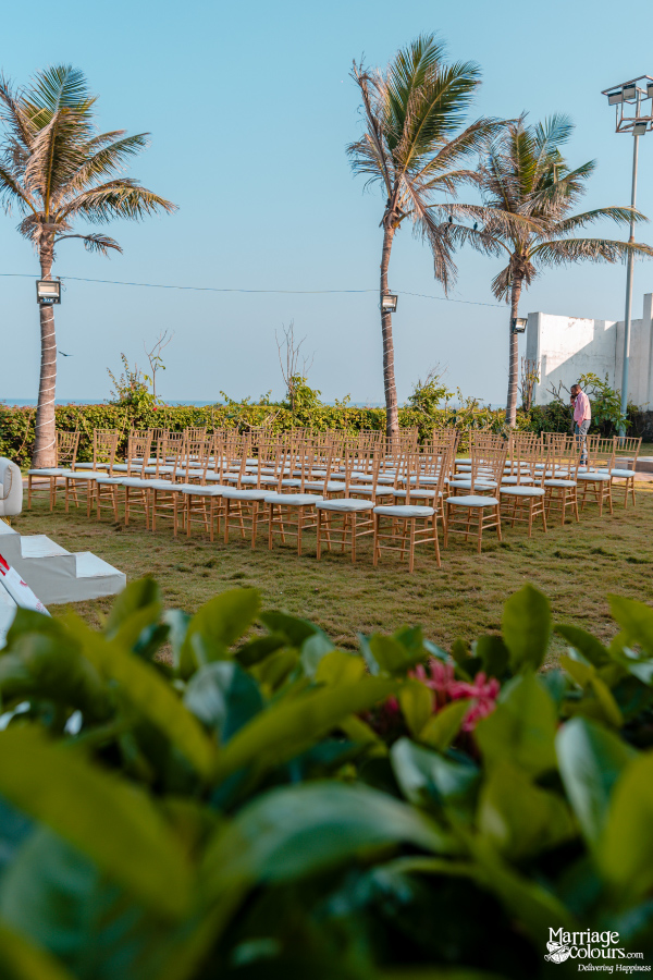 Outdoor ceremony seating on a lawn with gold chairs, palm trees, and ocean background.