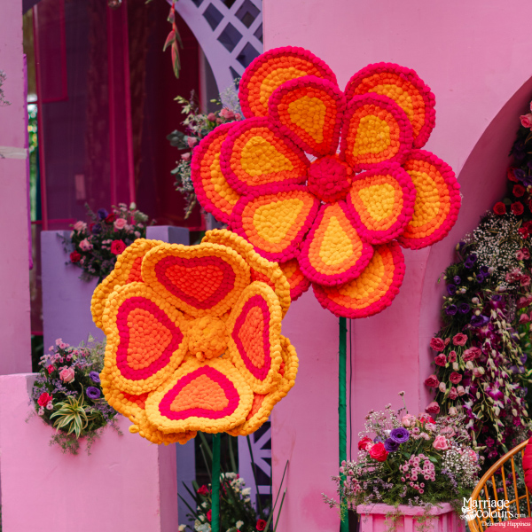 A vibrant, maximalist Indian wedding stage in shades of bright pink with oversized floral elements.