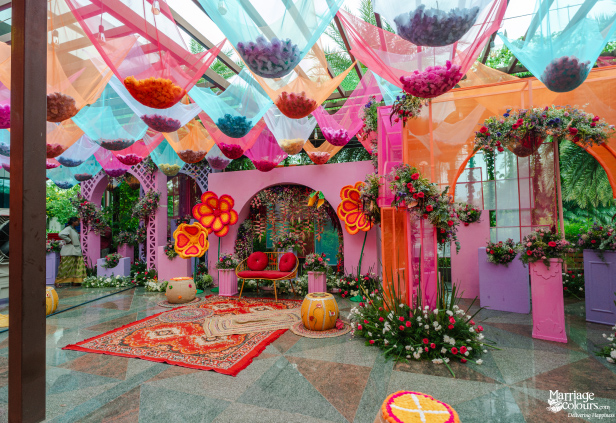 A highly decorated pink event space with a colorful canopy of hanging fabric pouches full of petals.