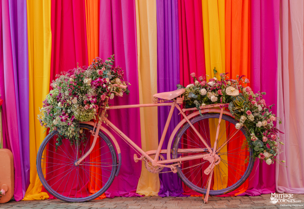 A vintage pink bicycle decorated with abundant pink, purple, and green fresh floral arrangements.