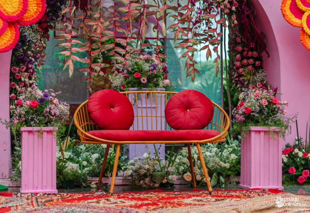 A stylish golden seating bench with red cushions, surrounded by lush floral arrangements and pink decor.