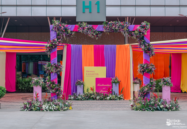 A vibrant floral archway and backdrop in pink, purple, and orange fabric outside a modern building entrance