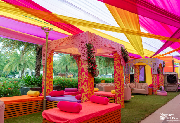 An outdoor lounge area with pink canopies, colorful seating, and a striking draped fabric ceiling.