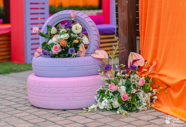 Two painted vehicle tires, lavender and pink, holding an arrangement of colorful fresh flowers.