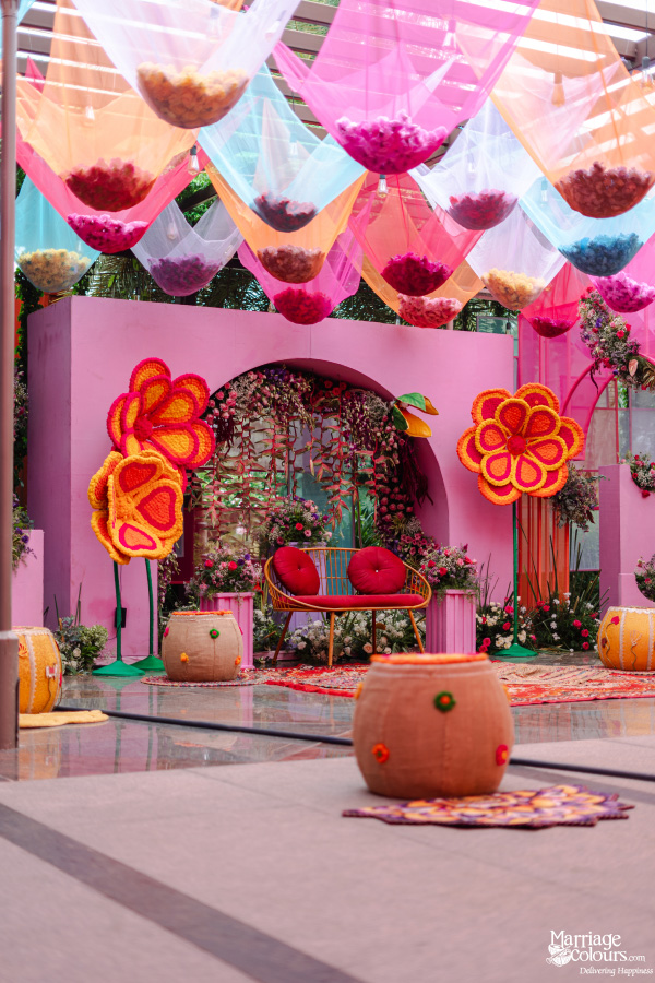 A vibrant, colorful event stage with pink backdrop, unique seating, and sheer fabric hanging decor.