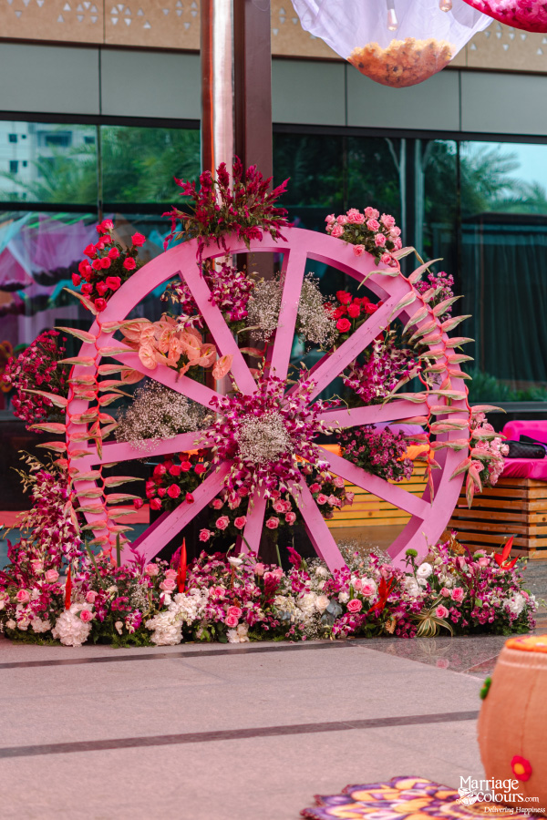 A large, pink wooden wheel decorated with rich magenta, pink, and white floral arrangements.