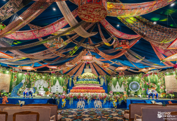 A grand, colorful banquet hall featuring a multi-tiered floral centerpiece, elaborate scenery, and patterned fabrics draped across the ceiling.